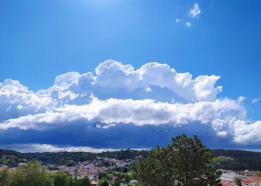 Büyüleyici bir kasabanın üzerinde dramatik bir gökyüzü. Dalgalanan bulutlar hava değişimlerine işaret ediyor, beklenti ve değişim hissi yaratıyor. Havayla ilgili içerik, seyahat blogları ve ilham verici tasarımlar için harika..