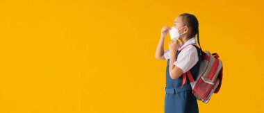 Okul afişi fikrine geri dönelim, Asyalı küçük kız tıbbi yüz maskesi takıyor, sarı arka planda izole edilmiş, tasarım yolları olan boş boş alan.