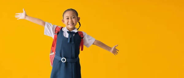 Back to school banner idea concept, Happy asian school girl in uniform with spreading hands joy and inspiration, isolated on yellow background with Clipping paths for design work empty free space