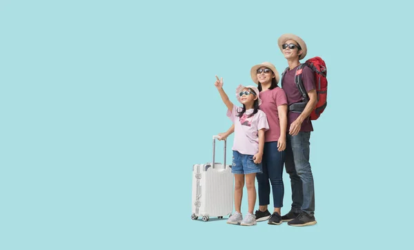 Family Travel Concept, Full body Happy asian family vacation, Father, mother and little daughter carrying  suitcases with hand pointing ready for vacation trip, isolated on pastel plain light blue