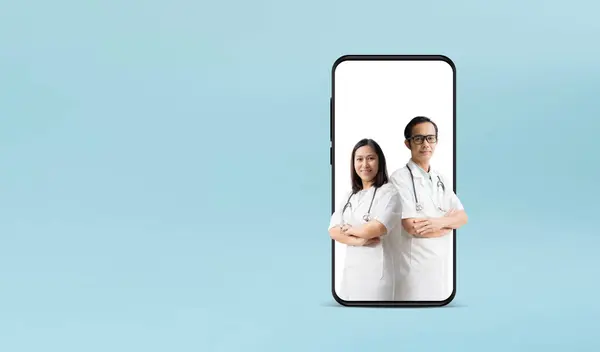 医疗服务 亚洲女医生和男医生手挽手 手持大大的智能手机 与蓝色背景隔离 免版税图库照片