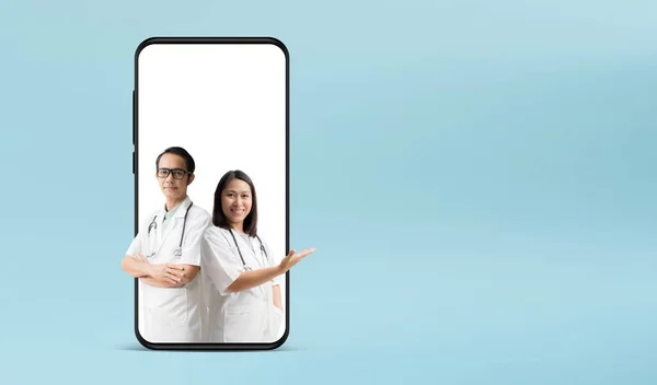 医疗服务 亚洲医生男女 手牵着手掌高举大智能手机 与蓝色背景隔离 图库图片