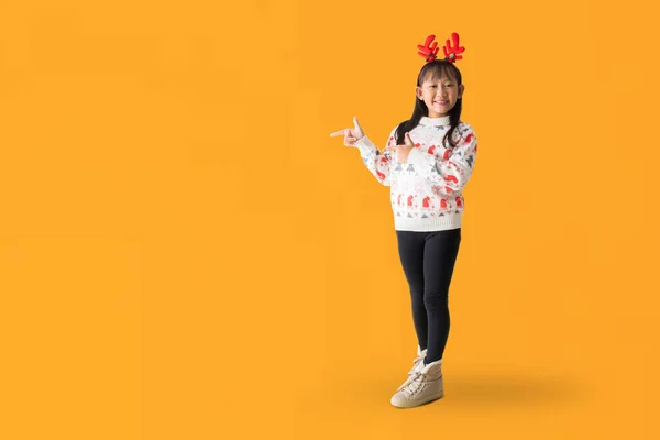 身穿圣诞毛衣 头戴驯鹿角的快乐的年轻亚洲女孩 高高兴兴地站在那里 手牵着手 摆出侧面的全身像 与白色背景隔离 为设计工作剪路 图库图片