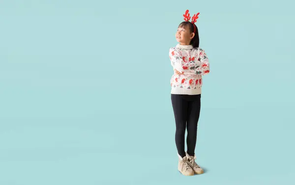 トナカイの角が付いているクリスマスのセーターを身に着けている陽気な若いアジアの少女 青い背景で隔離された完全なボディの肖像画をポーズする見て驚きの立っている幸せな笑顔 — ストック写真