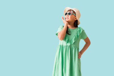 Mutlu gülümseyen Asyalı küçük kız şapka ve güneş gözlüğü pozu, moda yaz tatili konsepti, tüm vücut mavi arka planda izole edilmiş.