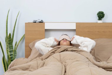 Göz maskesi takmış yatakta uyuyan genç bir kız tüm uyku ve rahatlama sahnesini örten bir battaniye.