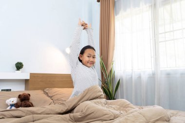 Uyan konsept, mutlu Asyalı genç Taylandlı kız sabahları yatağında uzanıyor, beyaz pijama giyiyor.