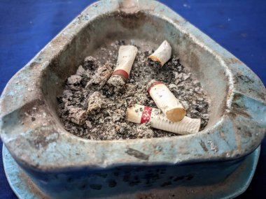 Üçgen bir kül tablasında birkaç sigara izmariti ve kül var.