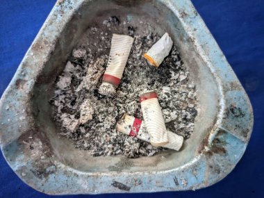 Üçgen bir kül tablasında birkaç sigara izmariti ve kül var.