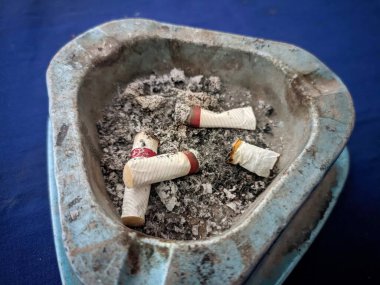 Üçgen bir kül tablasında birkaç sigara izmariti ve kül var.