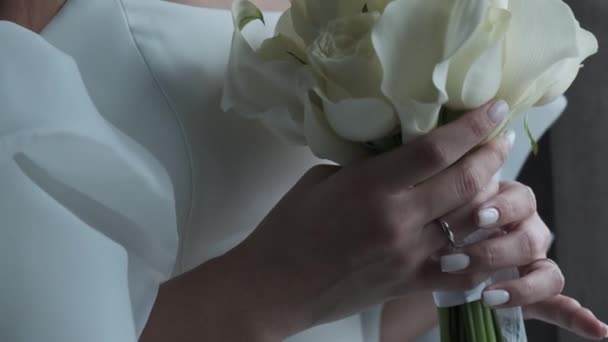 stock video  A bride in a gorgeous white chalet holds a bridal bouquet of white calla lilies. A close-up shot of her hand arranging the flowers.