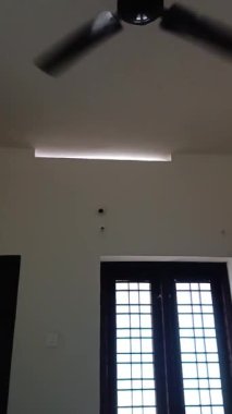 Beyaz duvarları ve tavanında vantilatörü olan bir oda.