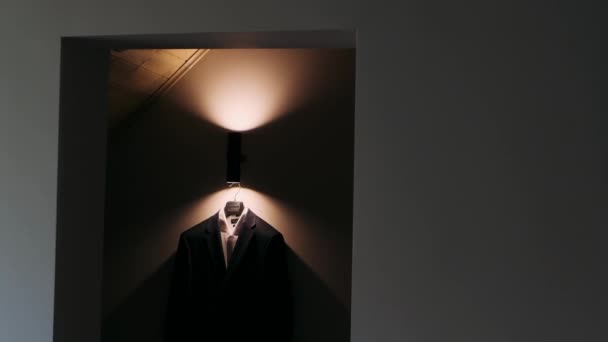 男のジャケットは暗い部屋のランプからの光の光線のハンガーに掛かります — ストック動画