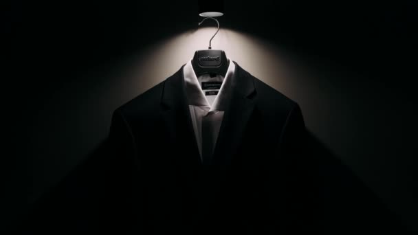 一个男人的夹克挂在衣架上 挂在黑暗房间里灯光下的衣架上 — 图库视频影像