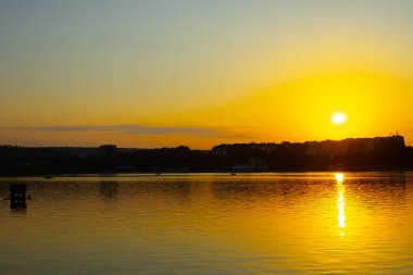 Gölün kıyısında gün batımı. Doğa manzarası. Yansıma, mavi gökyüzü ve sarı güneş ışığı. Gün batımında manzara.