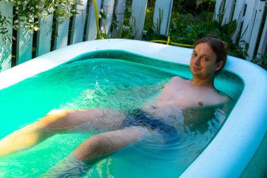 Mutlu ve güzel genç adam banyosu, su oynamak ya da büyük mavi taşınabilir yüzme havuzunda eğlenceli aktiviteler yapmak açık havada, arka bahçede ya da yaz akşamında. 