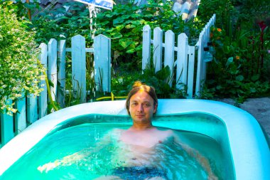 Mutlu ve güzel genç adam banyosu, su oynamak ya da büyük mavi taşınabilir yüzme havuzunda eğlenceli aktiviteler yapmak açık havada, arka bahçede ya da yaz akşamında. 