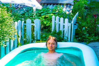 Mutlu ve güzel genç adam banyosu, su oynamak ya da büyük mavi taşınabilir yüzme havuzunda eğlenceli aktiviteler yapmak açık havada, arka bahçede ya da yaz akşamında. 