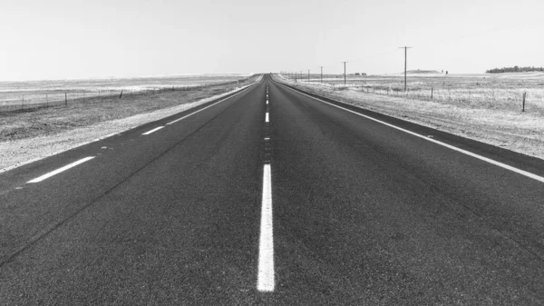Road Middle of Highway Straight horizon route black and white photograph through the rural countryside farming landscape a summer day.