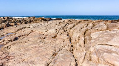 Ocean rocky beach coast with rock shelf ledge into calm sea blue sea water towards horizon landscape.