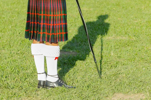 Scottish band musician drum major colours kilt  at highland games a rear view photograph outdoor field venue summer blue sky day.