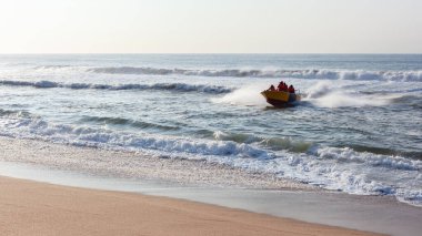 Köpekbalığı teknesi ve tanımlanamayan bakım ekibi okyanus dalgalarından kumsala doğru hızla iniyor. Sabah erken saatlerde, açık denizlerdeki banyo ağlarını kontrol ettikten sonra geri dönüyorlar..