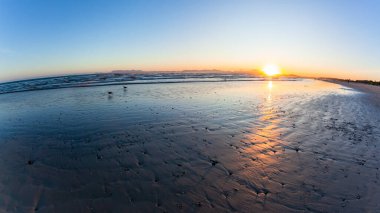 Beach ocean coastline as sun dipping water reflections behind mountains  a scenic lifestyle.