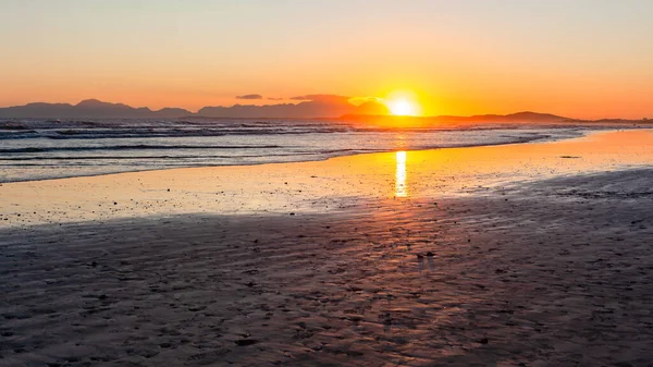 Beach ocean coastline as sun dipping water reflections behind mountains  a scenic lifestyle.