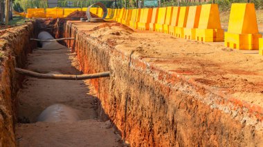Yeni çelik su borusu inşaatı yeraltı toprak işleri hendek inşaatı yakın plan mühendislik projesi. Sarı güvenlik engelli kırsal yol.