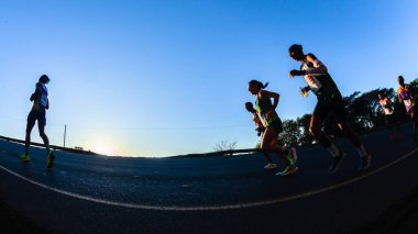 Maraton koşucuları siluet sabah şafak vakti şafak sökerken ultra mesafe yarışında yokuş yukarı koşuyor.