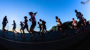 Maraton koşucuları siluet sabah şafak vakti şafak sökerken ultra mesafe yarışında yokuş yukarı koşuyor.