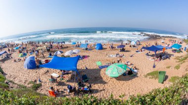 Plaj mavi deniz dalgaları tatil kalabalığı kumsalda güneşlenen insanlar perspektiften bakan bir tatil manzarası.