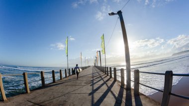 Young Surfer walking with surfboard on jetty platform a  rear behind action unrecognizable man silhouetted ocean entry off pier to go surfing. clipart