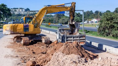 Endüstriyel inşaat karayolu genişletme ağır kazı makinesi açık mavi gökyüzü gününde toprak kumunu kamyona döktü..