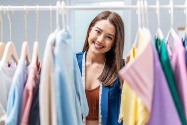 Moda mağazasındaki güzel kadın işyeri sahibi elbise demiryolundan kıyafet seçer, moda tasarımcısı müşterilere hizmet etmek için ayakta durur. Meslek Giysisi Tasarımcısı