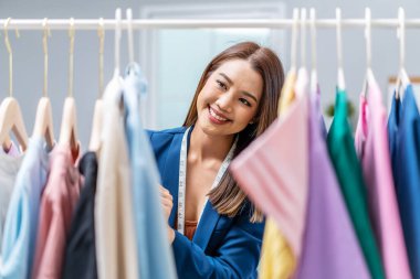 Moda mağazasındaki güzel kadın işyeri sahibi elbise demiryolundan kıyafet seçer, moda tasarımcısı müşterilere hizmet etmek için ayakta durur. Meslek Giysisi Tasarımcısı