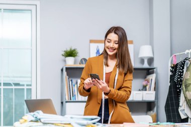 Müzakereler online. Ev ofis stüdyosundaki iş yerinde cep telefonu kullanan ilgi çekici genç kadın giysi tasarımcısı. Terzi müşteri müşteri tedarikçisini arıyor. Sipariş detaylarını görüşmek için.