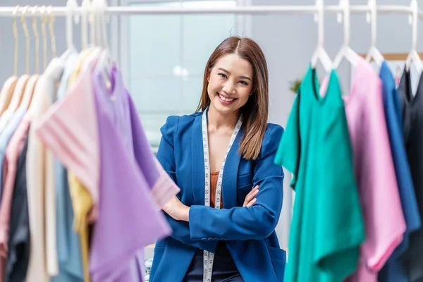 Beautiful woman business owner choose clothes in the clothes rail, Fashion designer standing and smile in cross arm gestures during working at fashion studio, Concept Professional Dressmaker designer