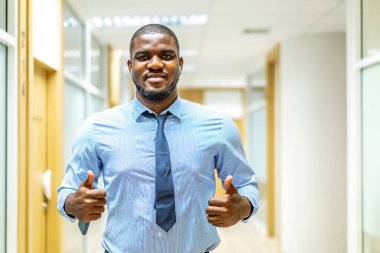 Gülümseyen olgun Afro-Amerikan yönetici iş adamının portresi kameraya bakarken modern koridor ofisinde poz veriyor, işaret veriyor, mutlu bir şekilde gülümsüyor