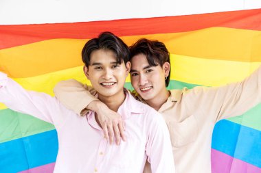 Mutlu eşcinsel çiftin portresi gökkuşağı bayrağıyla sevgilerini gösteriyor. Birbirini kollayan ve LGBTQ bayrağını tutan gülüyorlar, LGBT ve aşk konsepti..