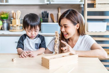 Genç Asyalı anne ve küçük oğlu evlerinin mutfağında ahşap yapboz oynamaya bayılıyorlar. Mutluluk, çocukluk ve annelik kavramına benziyorlar.