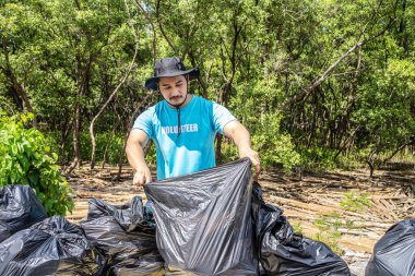 İş tulumlarında gönüllü olan biri çöpleri plastik torba içinde ormanda topluyor. Aksiyon sırasında yakın çekim. Doğayı atıktan temizlemek. Çevresel yardım. Ormanda çöp toplama