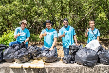 İş tulumlarında çalışan dört gönüllü, çöpleri plastik torba içinde ormanda topluyor. Aksiyon sırasında yakın çekim. Doğayı atıktan temizlemek. Çevresel yardım. Ormanda çöp toplama