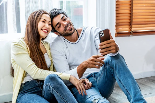 stock image Relaxed young interracial couple or friends using a generic mobile phone together sitting in the living room at home, Happy young man and woman with smartphone