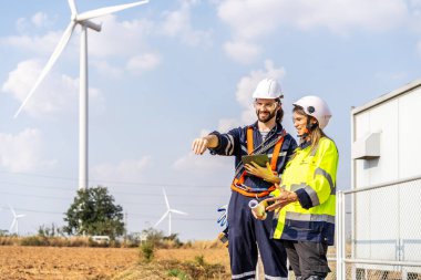 Kafkasyalı mühendis, iş arkadaşı kadınla tablet ve planlar üzerinde tartıştı. Yel değirmeni ya da rüzgar türbini önünde durdu. Rüzgar türbini elektrik üretti.