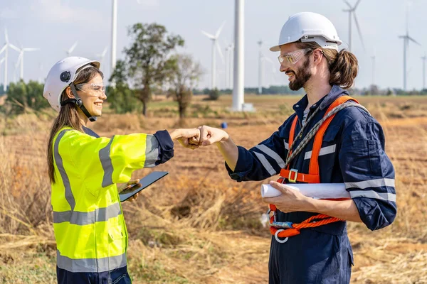 Caucasian man and woman engineers in uniform discuss with shaking hands stand near wind turbines ecological energy industry, Environmentally friendly for the future