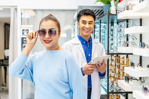 stock image Young asian man ophthalmologist present new collection of glasses to Customer, helping and selling senior woman in optical center, eye care concept, used correct assist or defective eyesight.