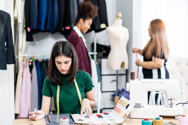 Beyaz kadın moda tasarımcısı, bir elbise tasarımı koleksiyonu için dijital tablet ve renkli kumaşlar çizerek, terzilik ve tasarım için kıyafet renklerini seçerek stüdyoda çalışıyor.