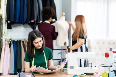 Beyaz kadın moda tasarımcısı, bir elbise tasarımı koleksiyonu için dijital tablet ve renkli kumaşlar çizerek, terzilik ve tasarım için kıyafet renklerini seçerek stüdyoda çalışıyor.