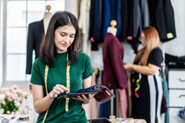 Gülümseyen beyaz kadın moda tasarımcısı stüdyoda çalışıyor elbise tasarım koleksiyonu için renkli kumaş seçiyor ve kameraya bakıyor, terzilik ve tasarım için kıyafet renklerini seçiyor.